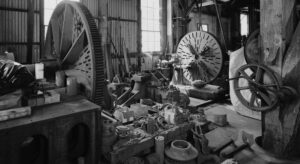 a black and white photo of a barn with old fashioned equipment and a large cog wheels inside